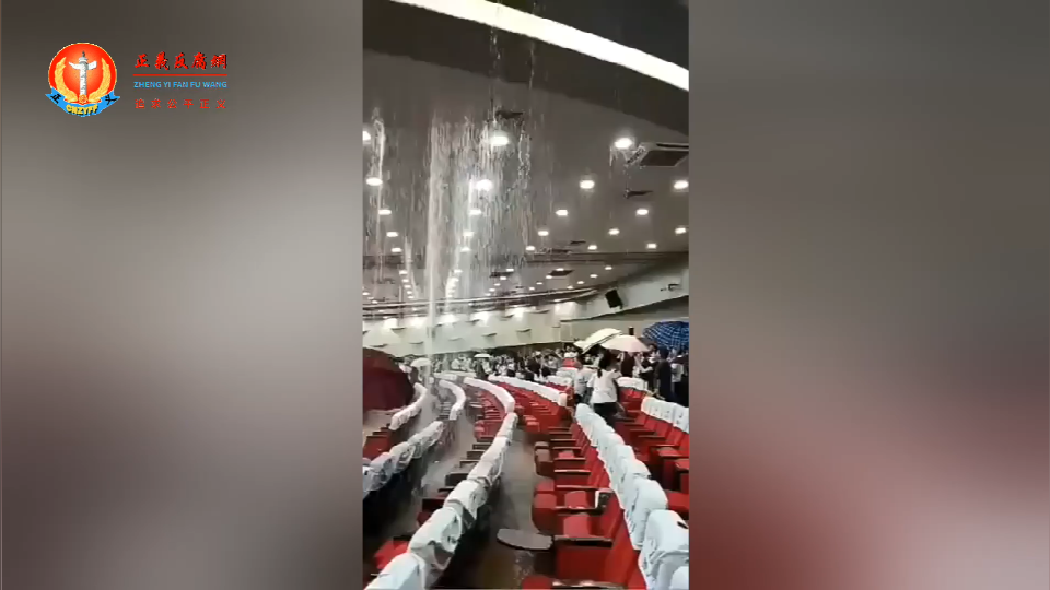 南京江北新区一个大礼堂里突然严重漏雨，观众席上参与活动的人员纷纷起身躲雨，许多人撑开了雨伞。.png