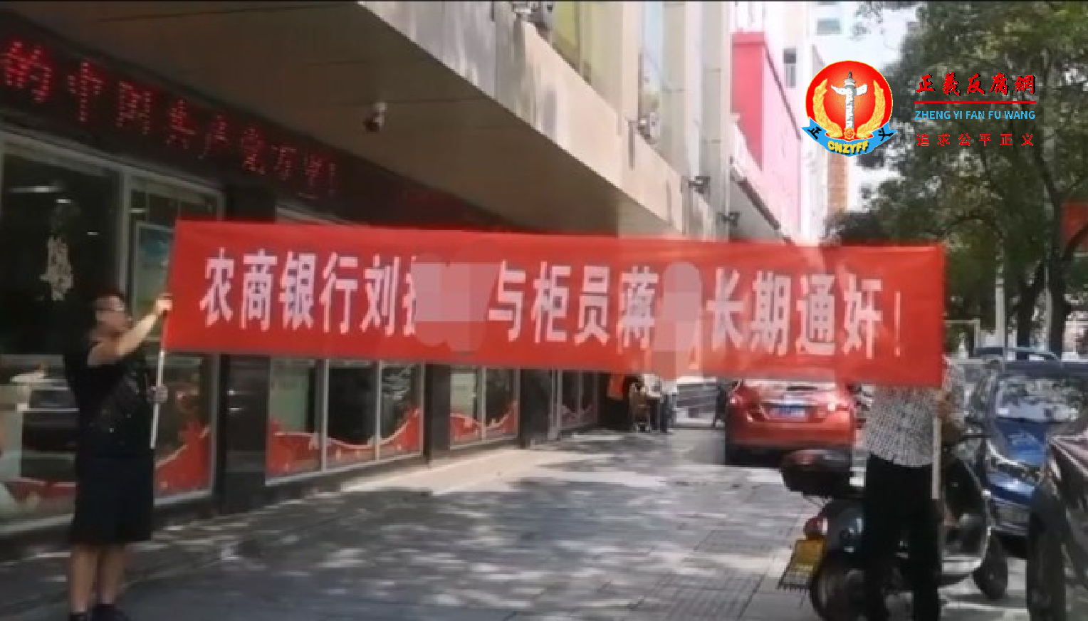 两名男子拉起横幅上面写着：农商银行刘振湘与柜员蒋雪长期通奸。.png